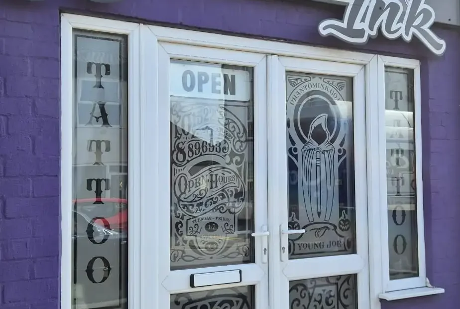 Storefront sign reads 'Phantom Ink' with skull emblem above a purple-tac storefront door.