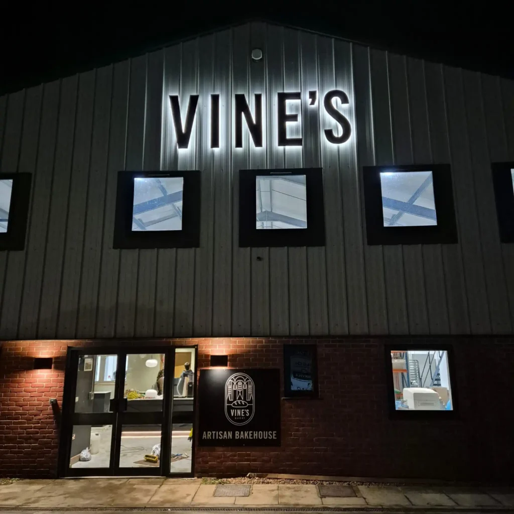 Nighttime exterior of Vine's Artisan Bakehouse with a brick facade and illuminated sign above the entrance.