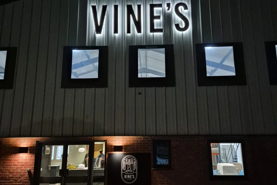 Nighttime exterior of Vine's Artisan Bakehouse with a brick facade and illuminated sign above the entrance.
