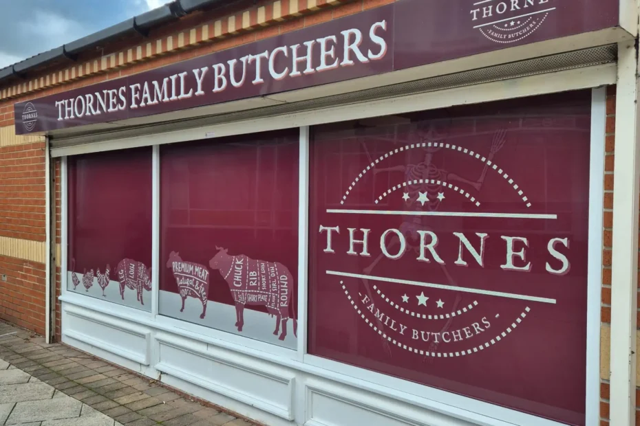 Storefront sign reading 'THORNES FAMILY BUTCHERS' with a circular Thornes logo on a maroon background beside large windows
