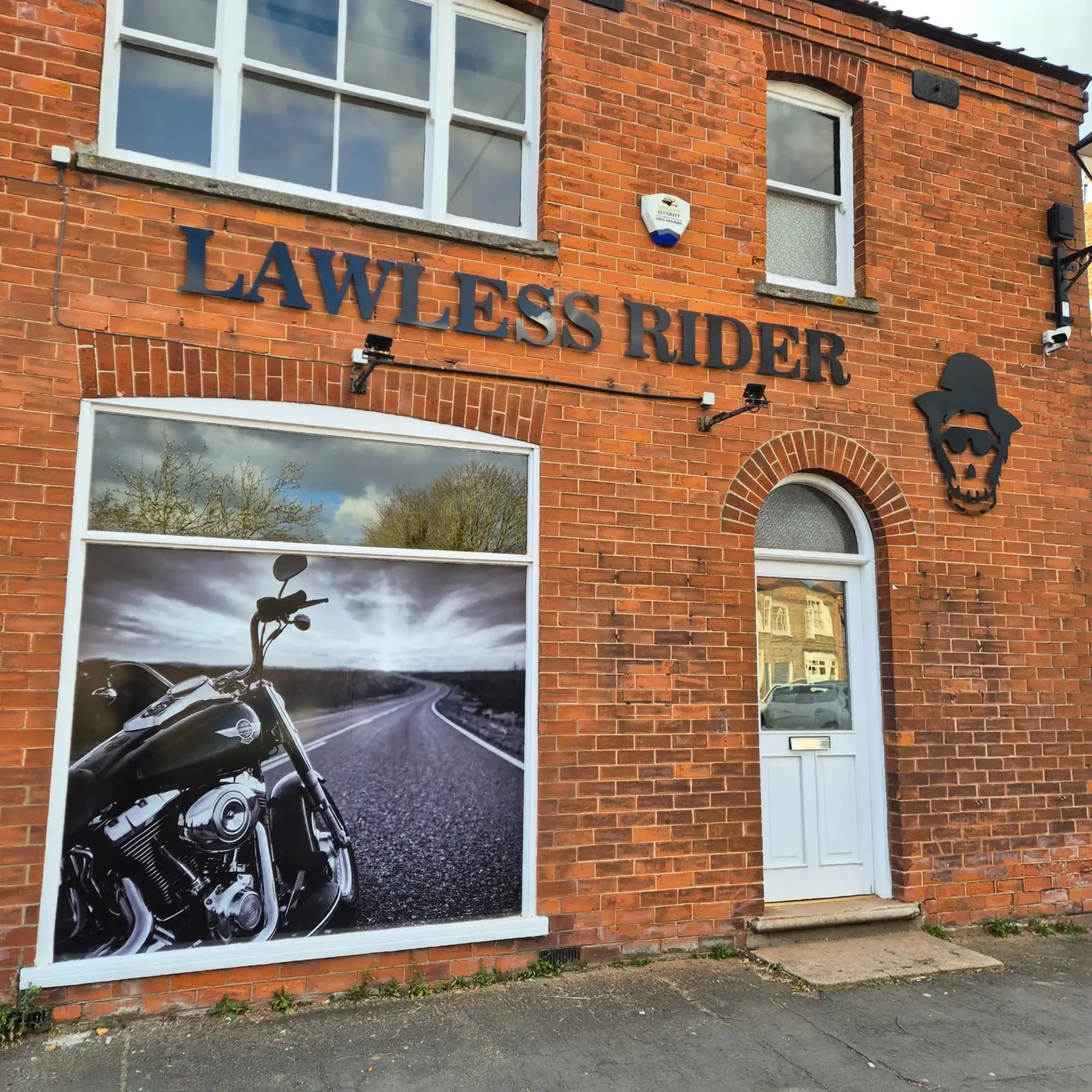 Brick storefront with a large motorcycle poster in the front window and the blue sign 'LAWLESS RIDER' across the brick wall above.