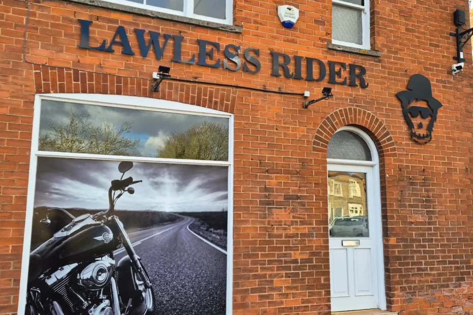 Brick storefront with a large motorcycle poster in the front window and the blue sign 'LAWLESS RIDER' across the brick wall above.