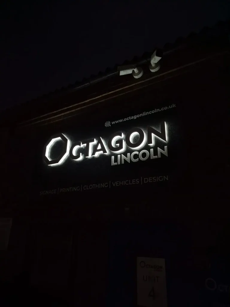 Nighttime storefront of Octagon Lincoln with an illuminated logo sign on a dark building exterior.