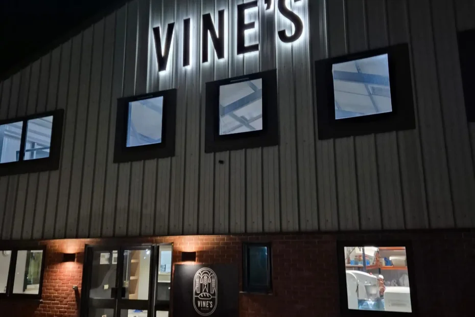 Night exterior of a brick bakery building with illuminated 'VINE'S' sign and 'ARTISAN BAKEHOUSE' logo near the entrance.