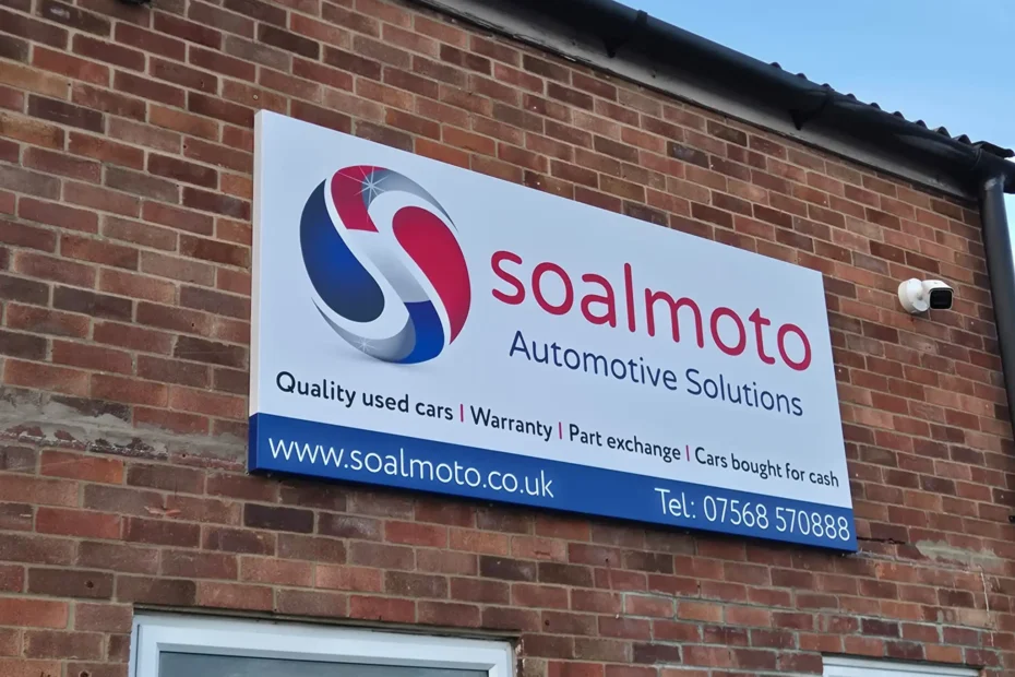 Exterior view of a brick building with a large Soalmoto Automotive Solutions sign and a red‑blue swirl logo on the wall.